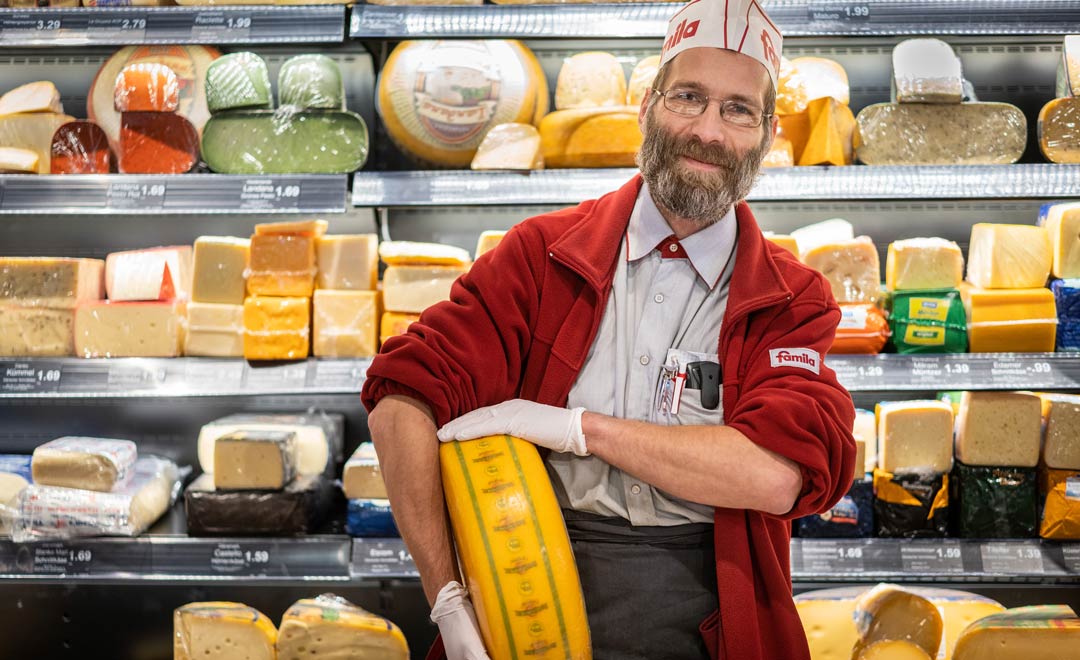 Vendeur avec une meule de fromage devant le rayon fromagerie. 